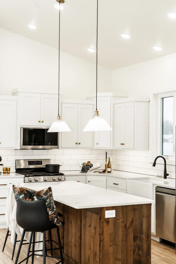 Modern kitchen with white cabinetry, stainless steel appliances, and a large island featuring a wooden base, complemented by pendant lighting and stylish bar stools.