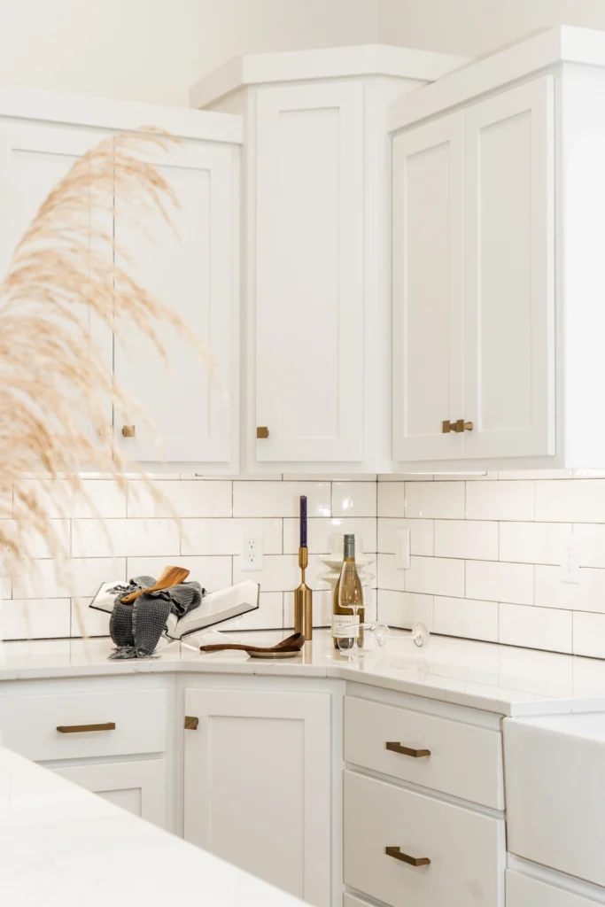 Modern kitchen corner featuring white cabinetry, marble countertops, decorative items including a wine bottle, candle holder, and utensils, with a touch of natural decor from dried pampas grass.