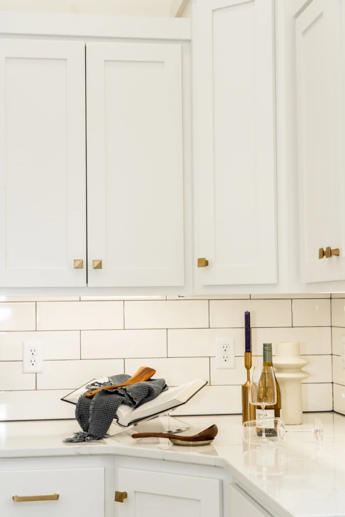 Modern kitchen with white cabinetry, marble countertop, kitchen utensils, wine bottles, and decorative accents, showcasing a stylish and functional design for custom homes in Fargo-Moorhead.