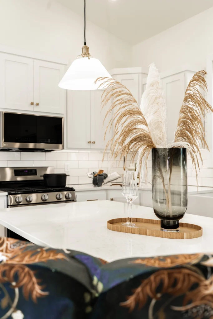 Modern kitchen interior featuring white cabinetry, a pendant light, and decorative dried grasses in a vase on a marble countertop, highlighting a stylish and inviting space for custom home design.