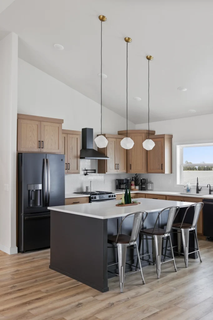 Modern kitchen featuring an island with metal stools, wooden cabinetry, pendant lighting, and stainless steel appliances, showcasing custom home design by Paragon Homes in Fargo, ND.