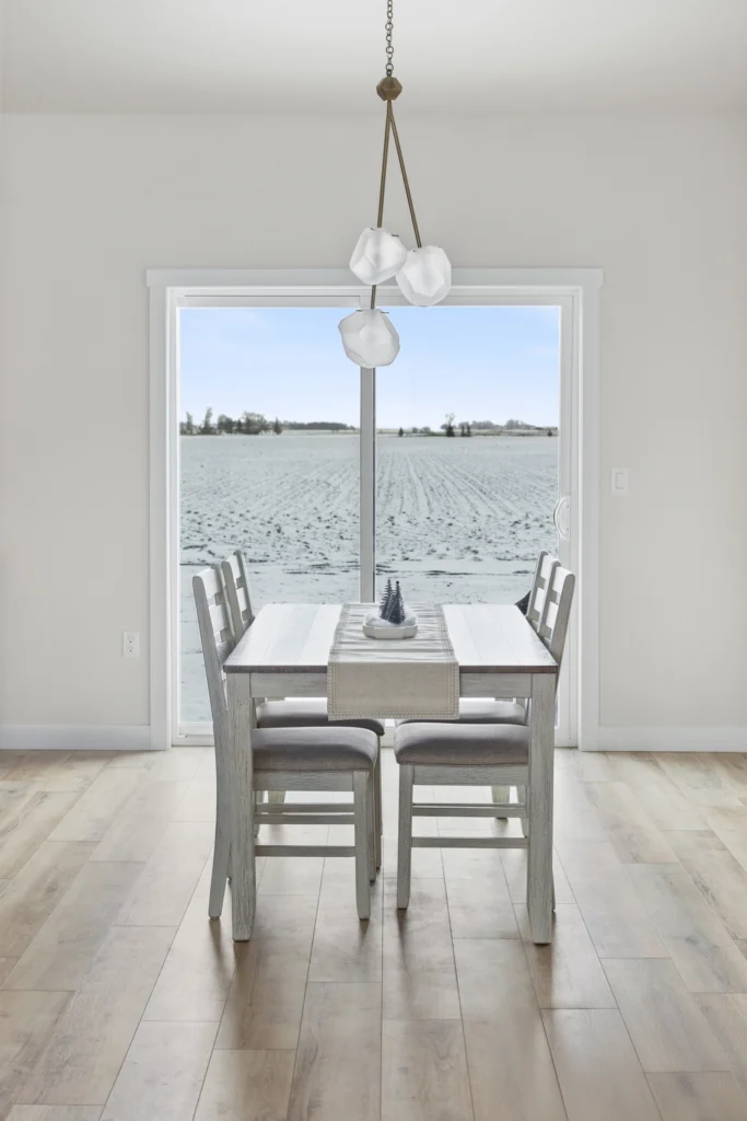Modern dining area with a wooden table and chairs, featuring a decorative centerpiece, large window showcasing a snowy landscape, and contemporary pendant lighting, reflecting Paragon Homes' custom design aesthetic in Fargo-Moorhead.