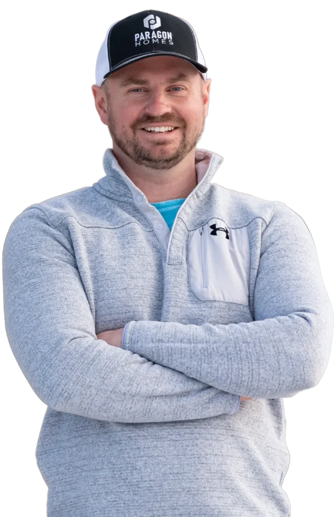 Mark Singleton, founder of Paragon Homes, smiling with arms crossed, wearing a gray fleece and a Paragon Homes cap, representing commitment to custom home building in Fargo, ND.